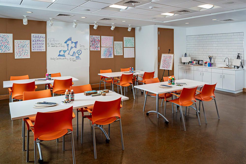 A modern classroom setup with orange chairs and white tables, designed for educational activities in a bright and organized space.