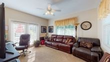A cozy living room with a leather sofa, ceiling fan, and large window with curtains.