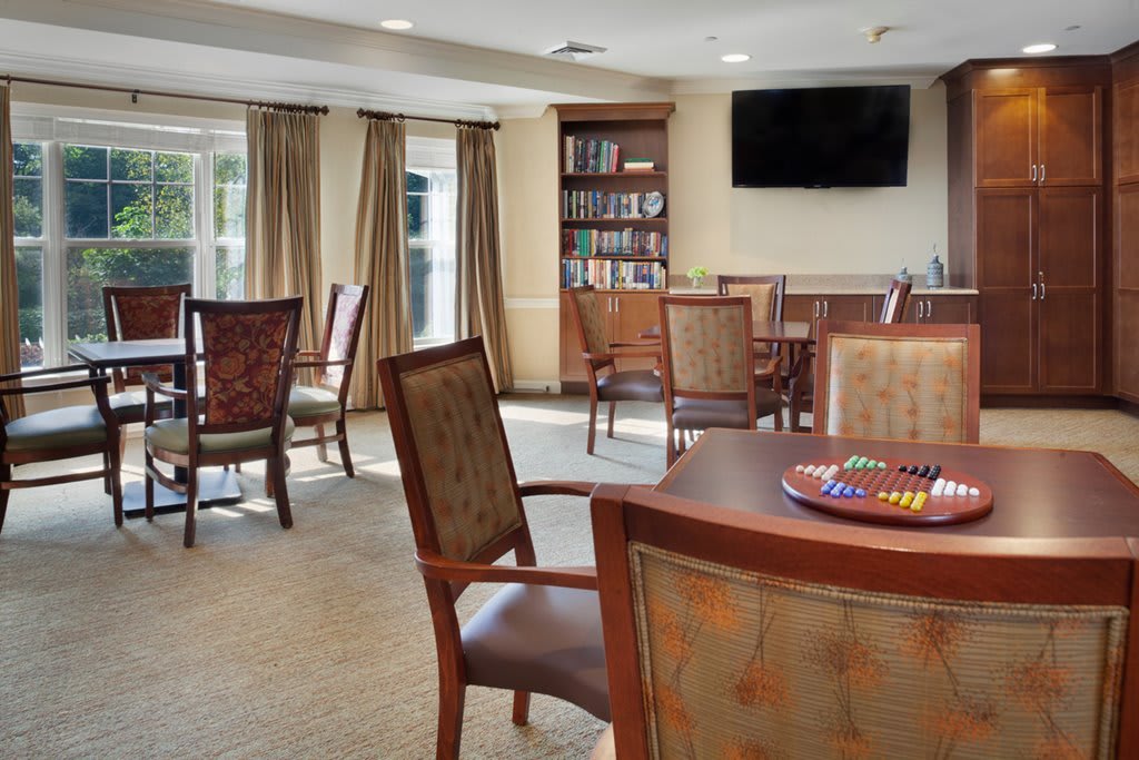 A cozy living room with several chairs and tables, a bookshelf, and a wall-mounted television.