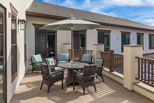 A cozy outdoor patio with a table, chairs, and an umbrella set on a deck.