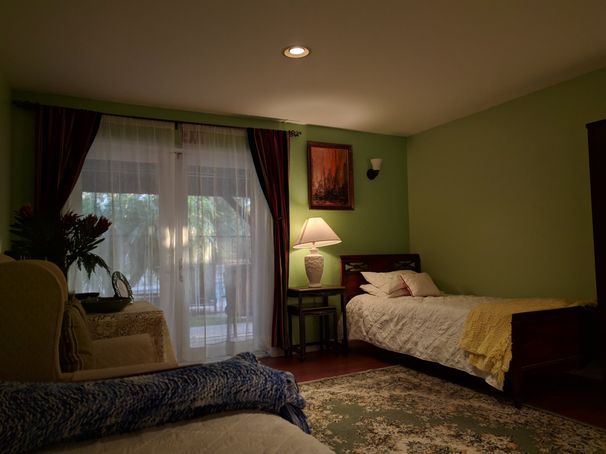 A cozy bedroom featuring twin beds, an armchair, soft lighting, and elegant curtains.
