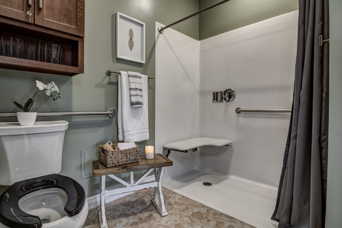 An accessible bathroom featuring a shower with grab bars and a folding seat, alongside a toilet and neatly arranged towels.