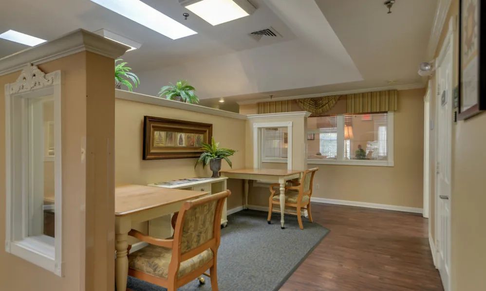 A cozy and well-lit office workspace with desks, chairs, plants, and wall artwork.
