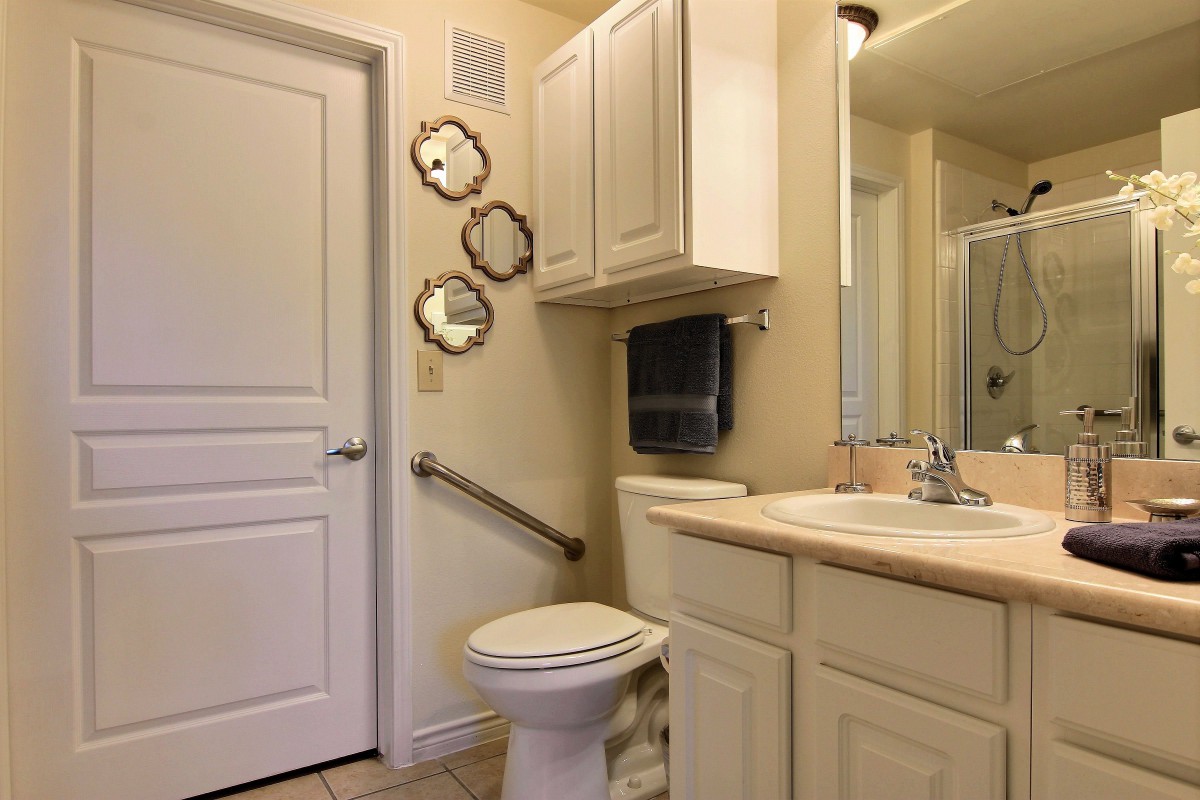 A clean bathroom featuring a toilet, sink, and wall-mounted cabinets with decorative mirrors.