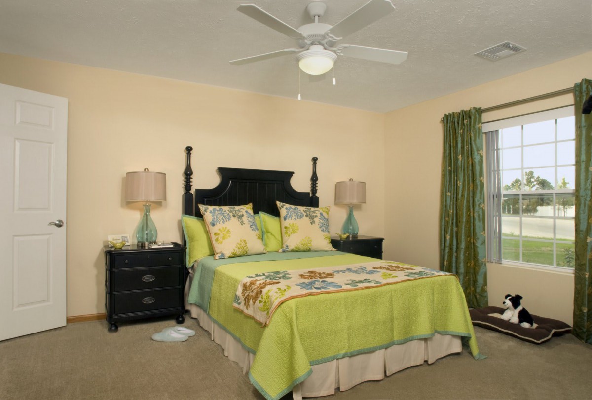 A cozy bedroom with green-themed bedding and curtains, featuring a dark wooden bed frame and matching nightstands, illuminated by table lamps.