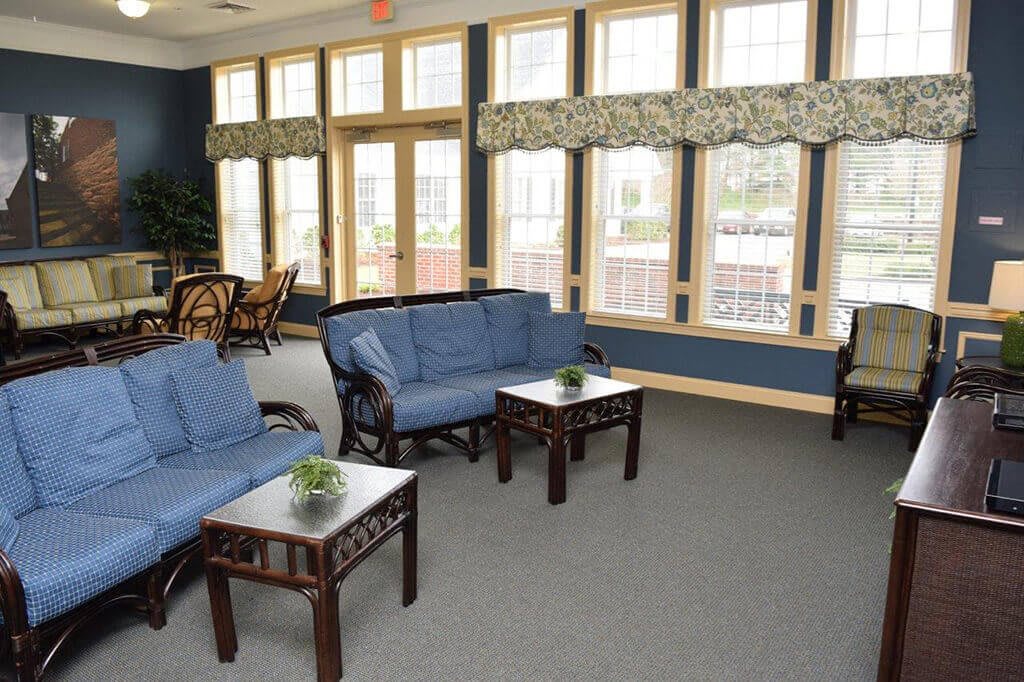 A cozy living room with blue sofas, wooden coffee tables, and large windows.