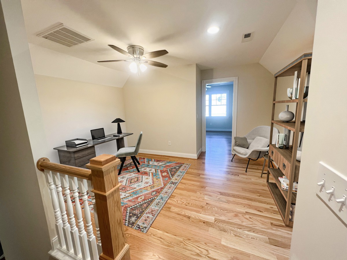 A cozy home office space with a desk, chair, and bookshelf, featuring a hardwood floor and ceiling fan.