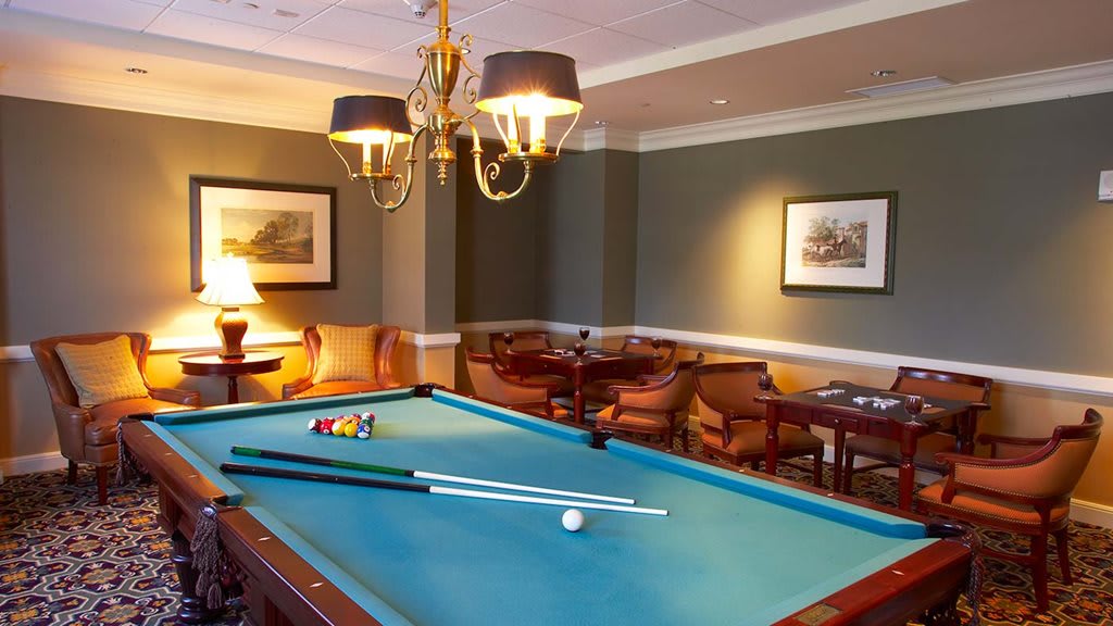 A cozy room featuring a pool table with cue sticks, seating area, and elegant lighting.