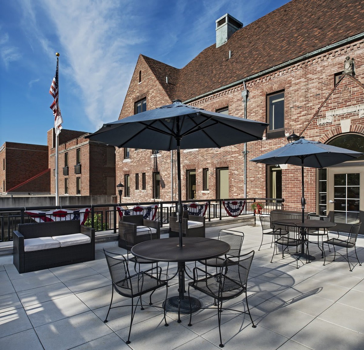 A charming patio with tables and umbrellas set against a brick building under a clear blue sky.