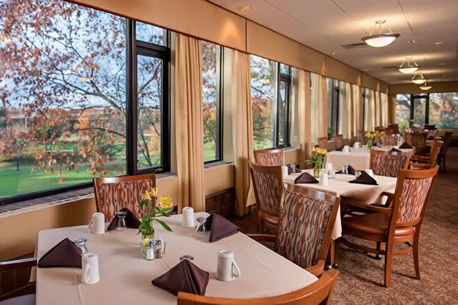 A restaurant dining area with elegantly set tables, large windows, and a view of the outdoors.