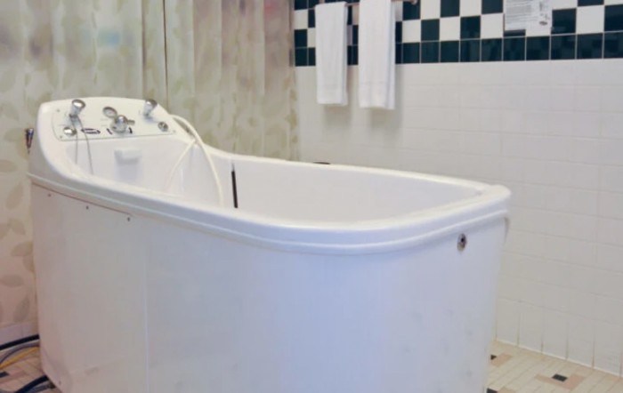 A bathroom featuring a white bathtub with checkered tile accents and towels hanging on the wall.