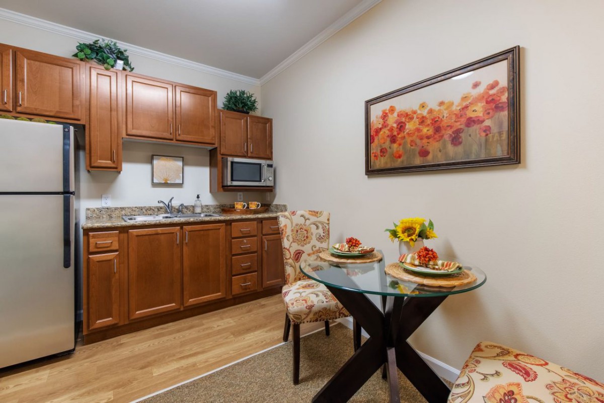 A cozy kitchen and dining area featuring wood cabinets, a small dining table set for two, and a decorative painting on the wall.