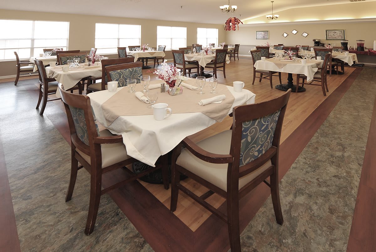A well-arranged dining area with tables set for service, featuring white tablecloths and neatly arranged chairs.