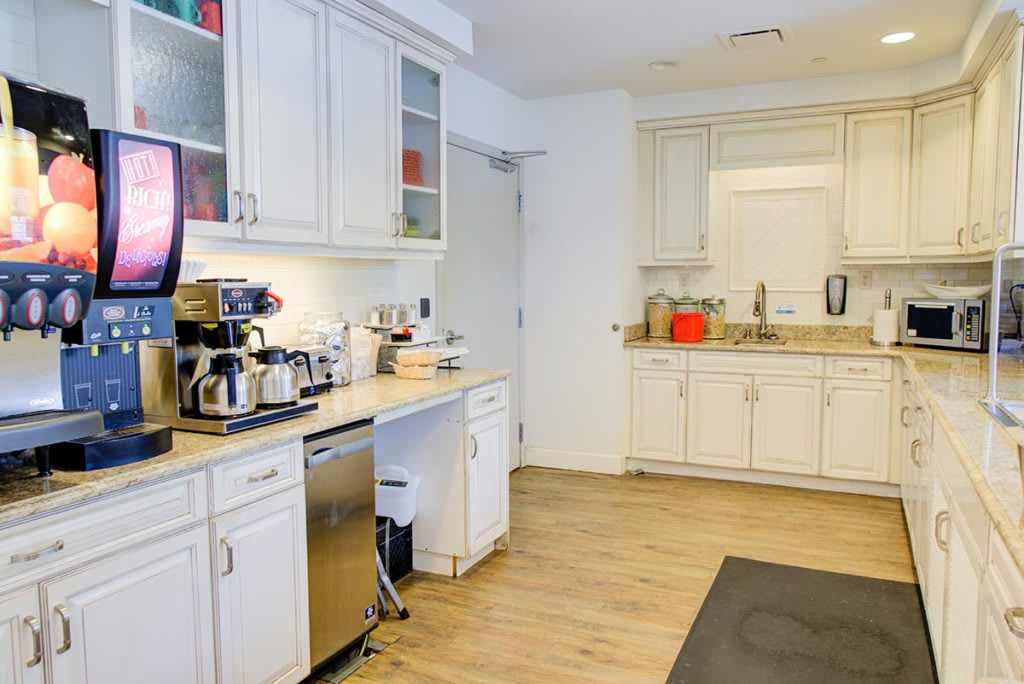 A modern kitchen with white cabinets, a coffee maker on the countertop, and a wooden floor.