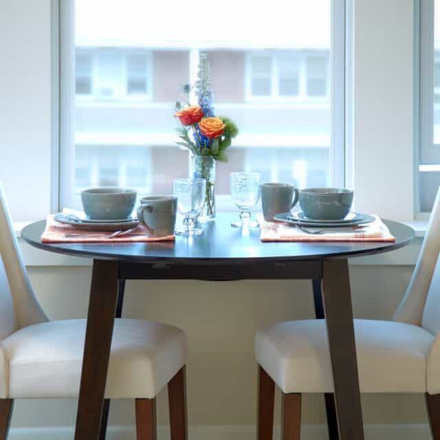 A cozy dining table set for two, featuring ceramic bowls and a vase of flowers by the window.