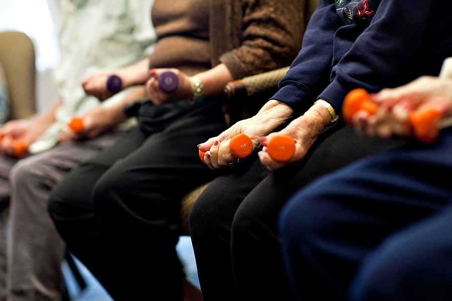 A group of seniors participating in a seated exercise session using small hand weights.
