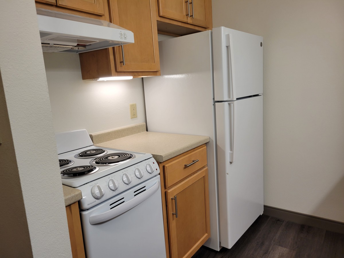 A compact kitchen with a stove, refrigerator, and wooden cabinets.