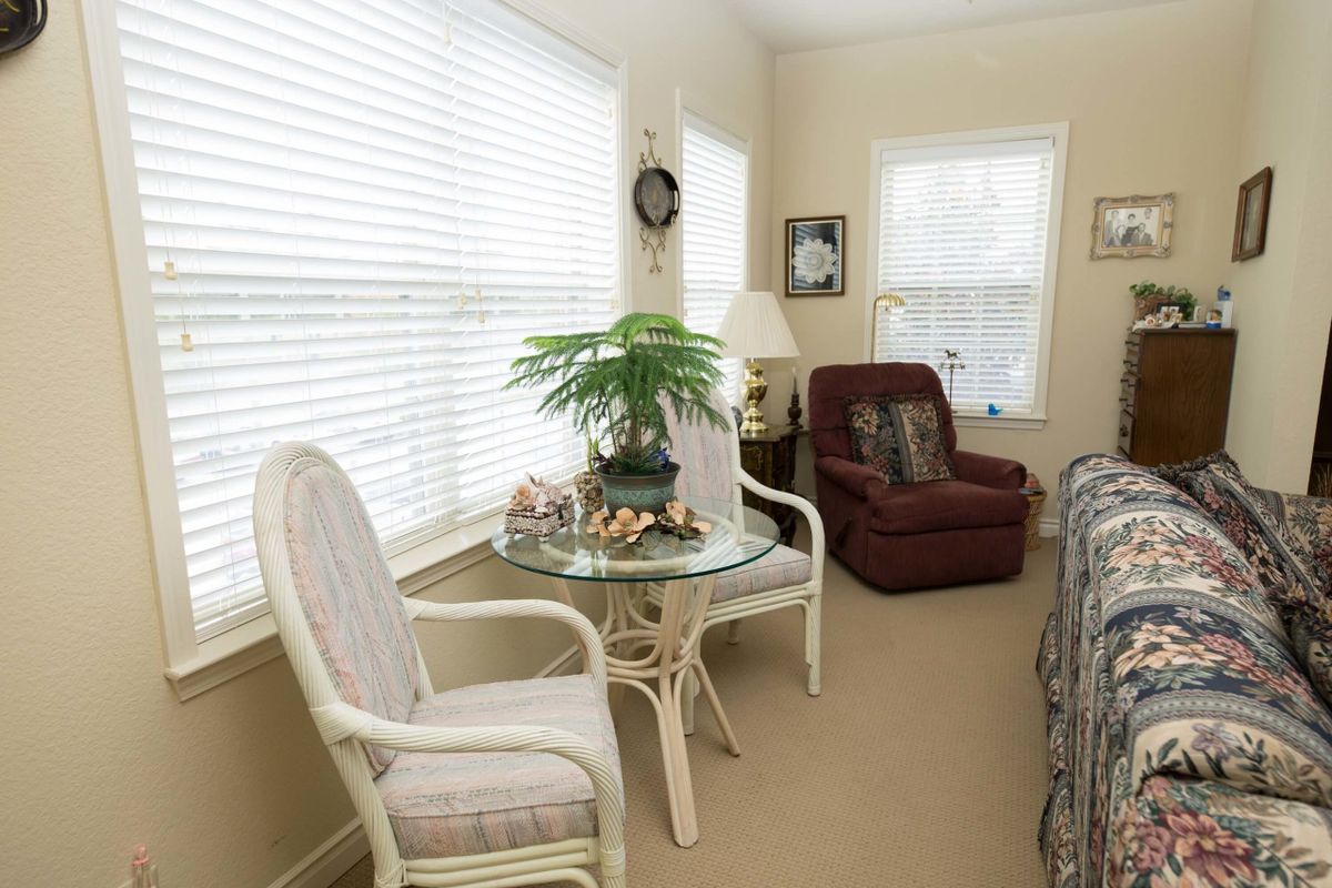A cozy living room with a glass table, chairs, and a plant by the window.