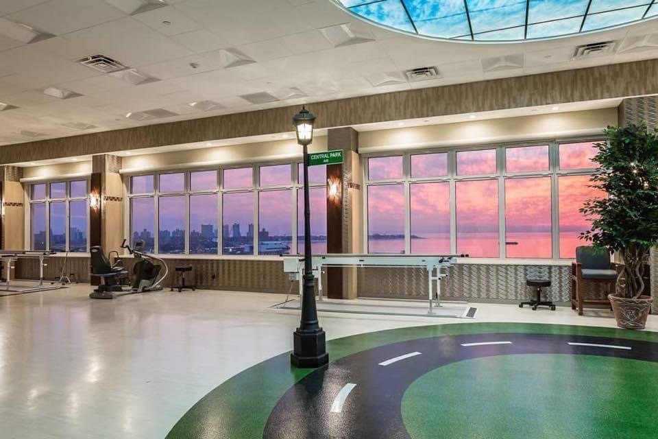 An indoor rehabilitation center with large windows showcasing a vibrant sunset, featuring a therapy track and a decorative lamp post.