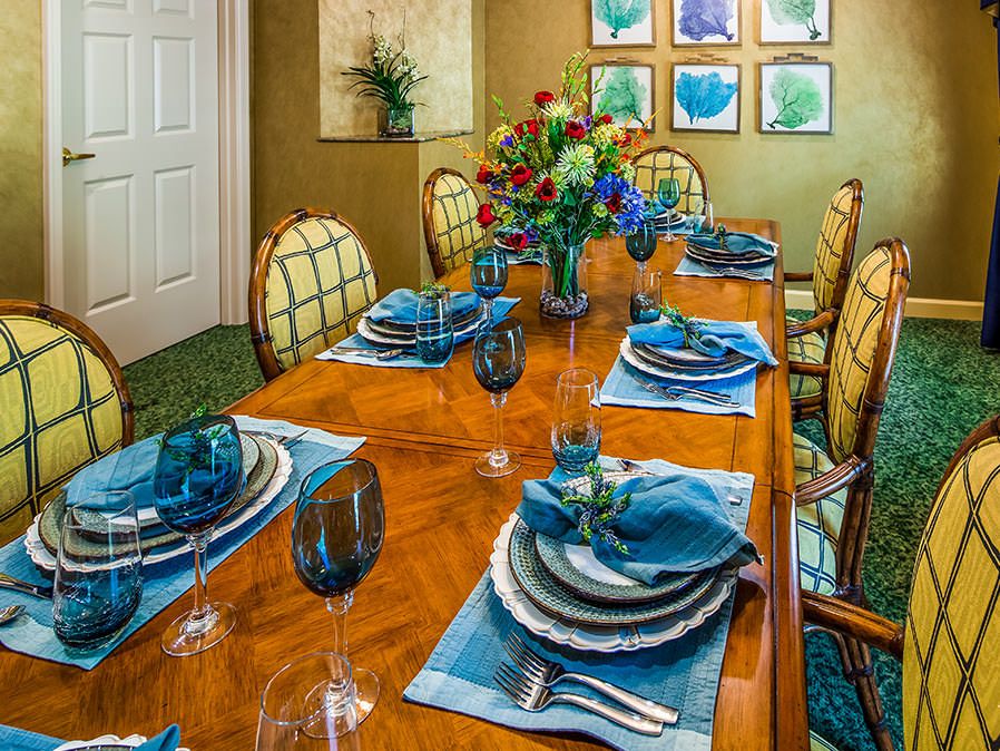 An elegantly set dining table with a blue-themed decor, featuring glassware, plates, and a floral arrangement.
