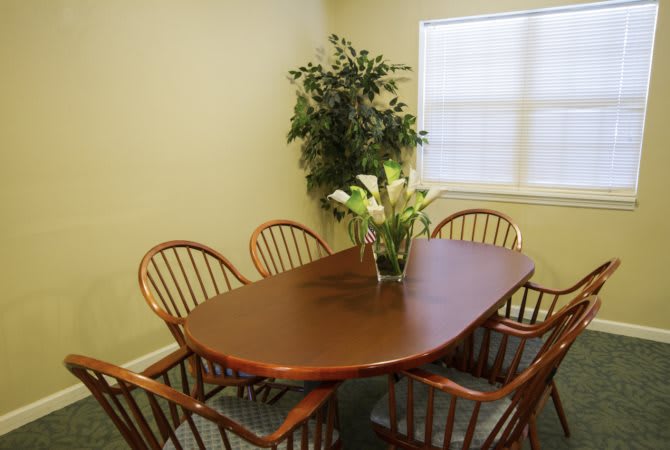 A dining room with a wooden table surrounded by chairs, featuring an indoor plant and flowers on the table.
