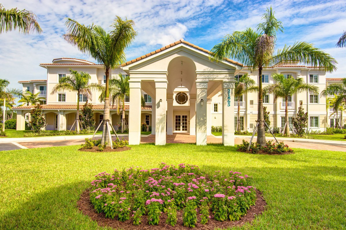 A beautifully landscaped residential complex with palm trees and vibrant flowers under a bright blue sky.