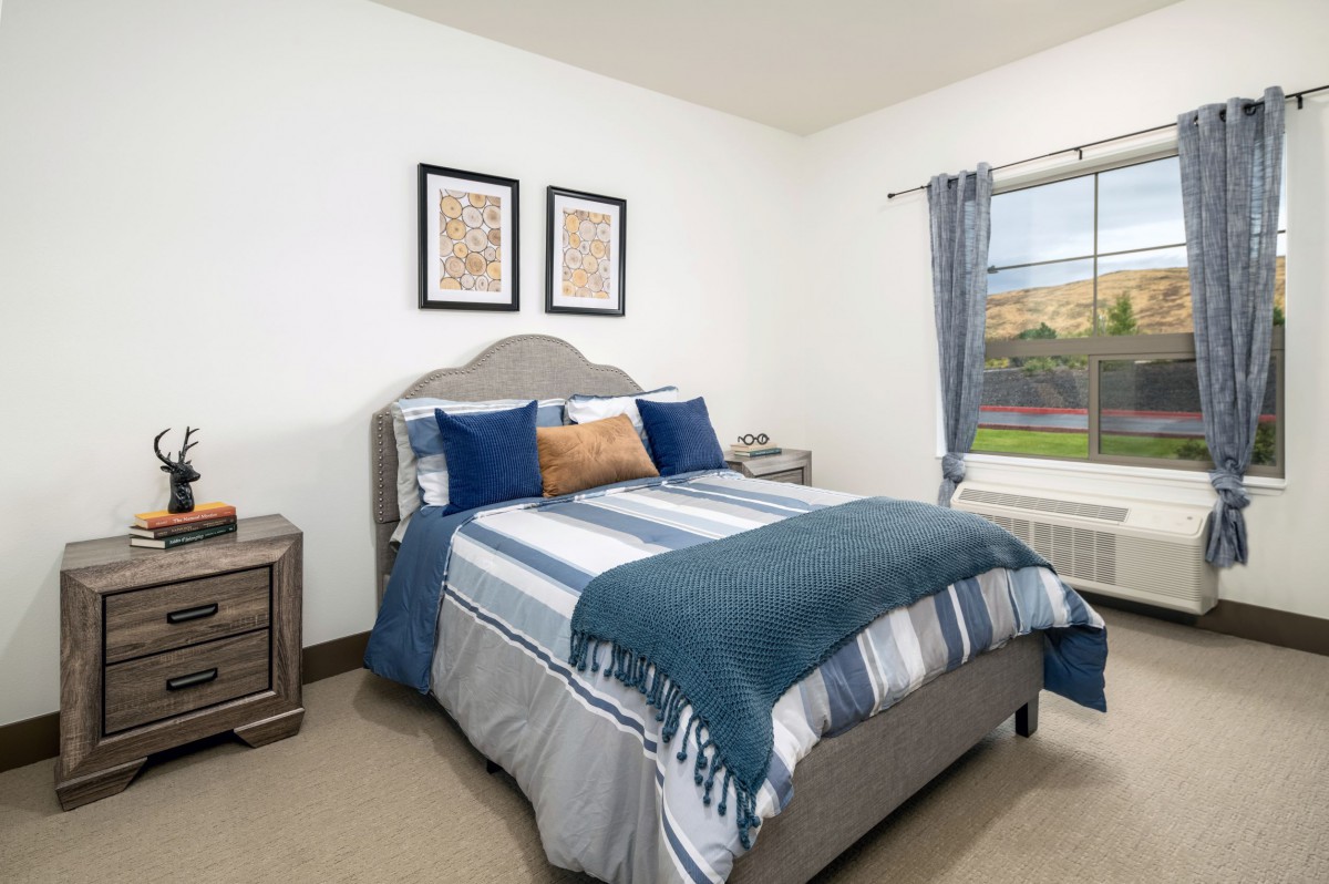 A cozy bedroom featuring a neatly made bed with striped bedding, complemented by blue and gray pillows, side tables, and wall art.