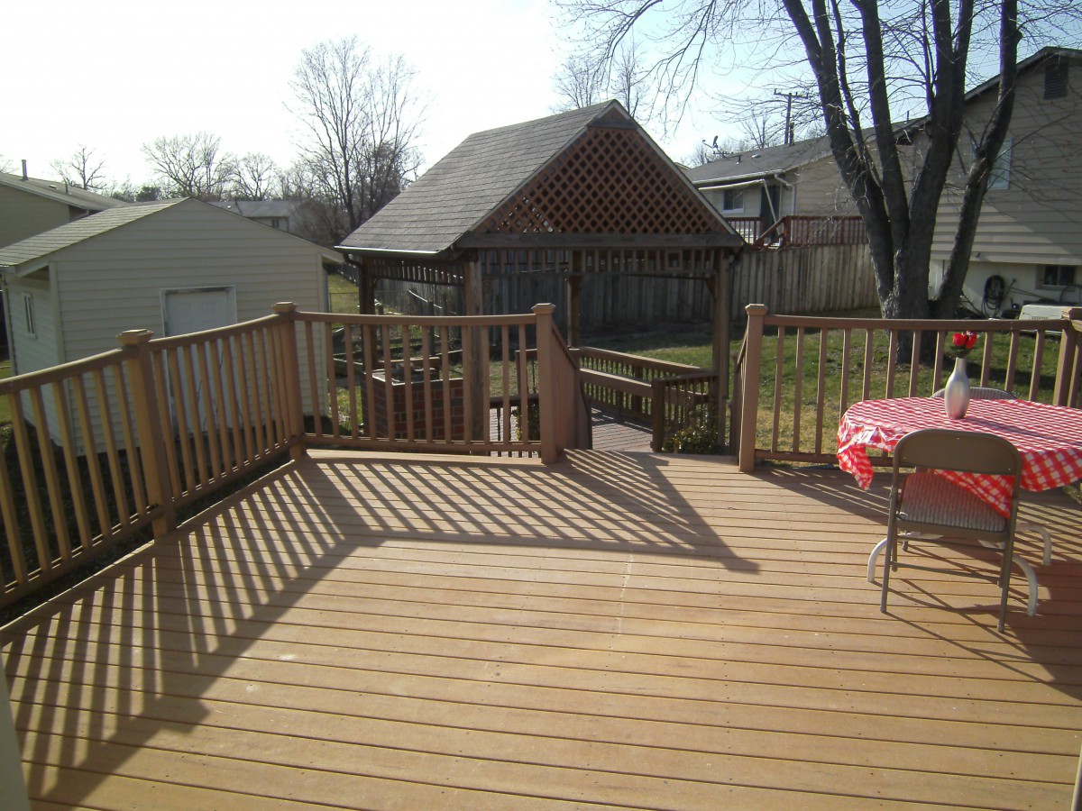 A sunny day on a wooden deck overlooking a backyard with a gazebo and fence.