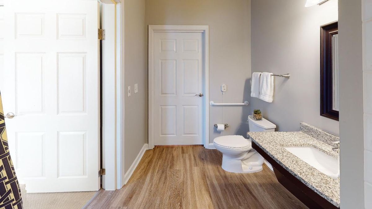 A modern bathroom with a toilet, sink, towel rack, and wooden flooring.