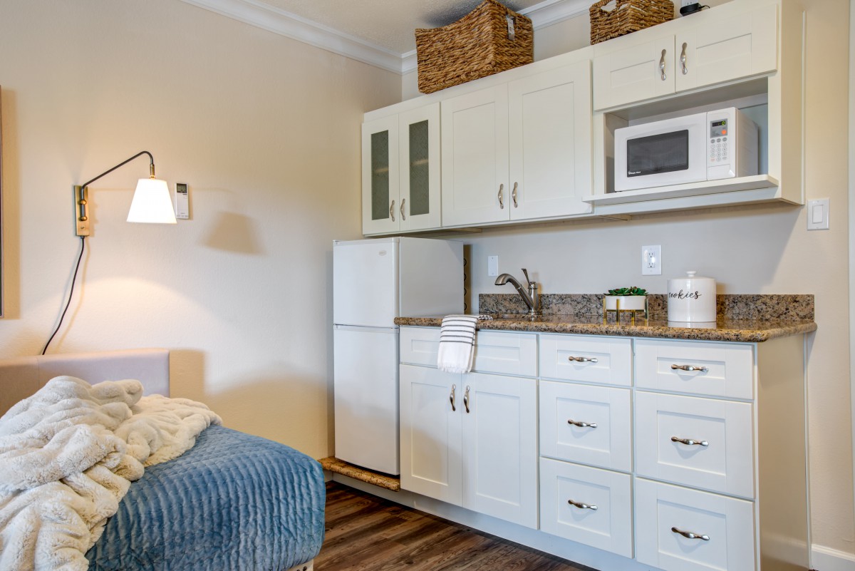 A compact and modern kitchen area in an apartment with white cabinets, a refrigerator, microwave, and sink.