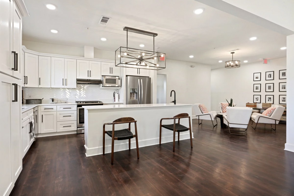 A modern open-concept kitchen with white cabinetry, hardwood floors, and stainless steel appliances.