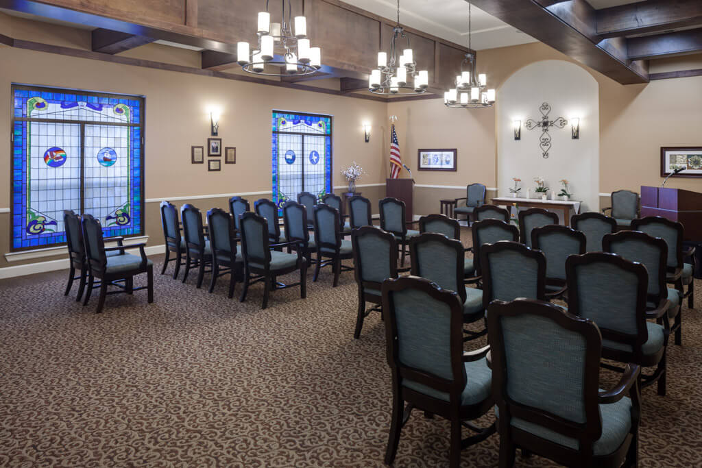 A neatly arranged meeting room with chandeliers, a pulpit, and stained glass windows.