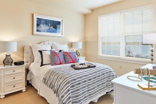 A cozy bedroom with a neatly made bed, decorated pillows, and natural light streaming in through a window.