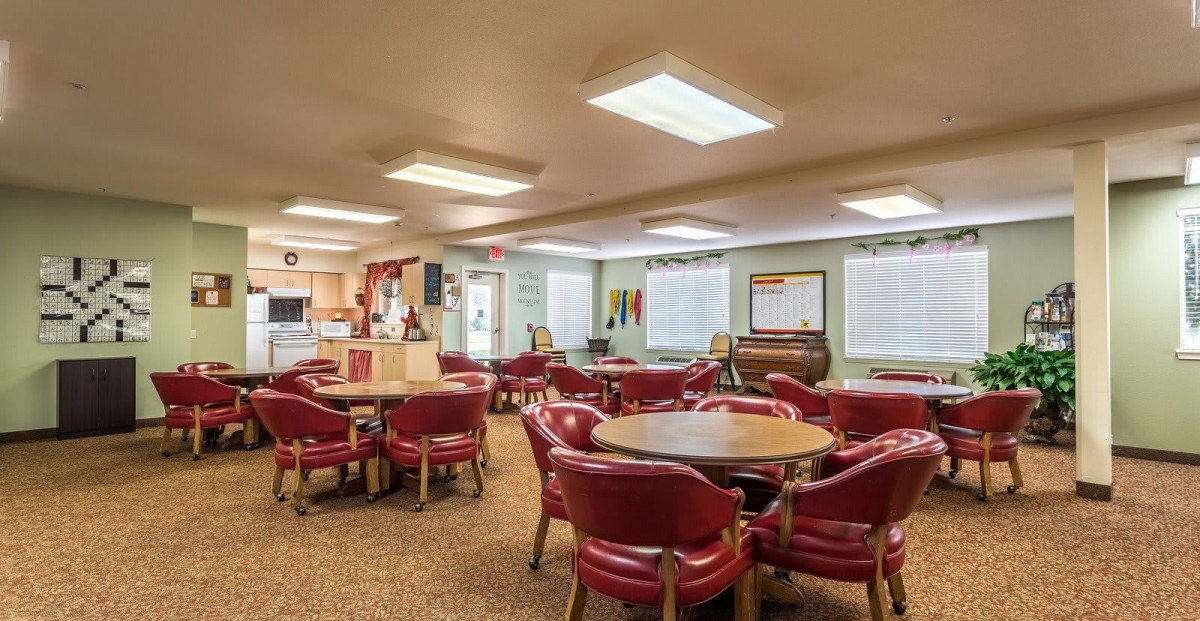 A cozy lounge area with red chairs and round tables, well-lit and carpeted.