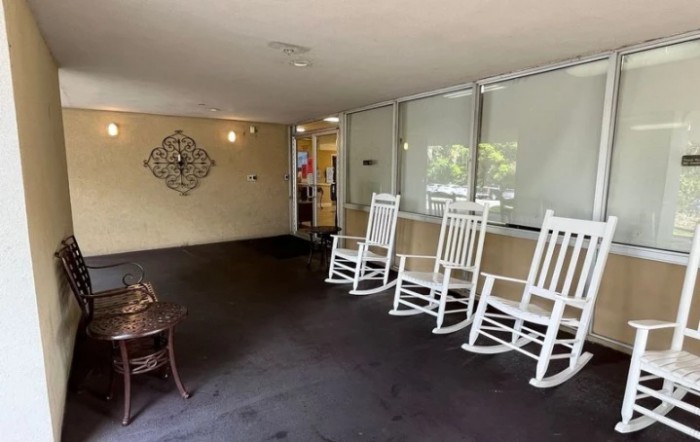 A cozy outdoor seating area with white rocking chairs lined up on a porch.