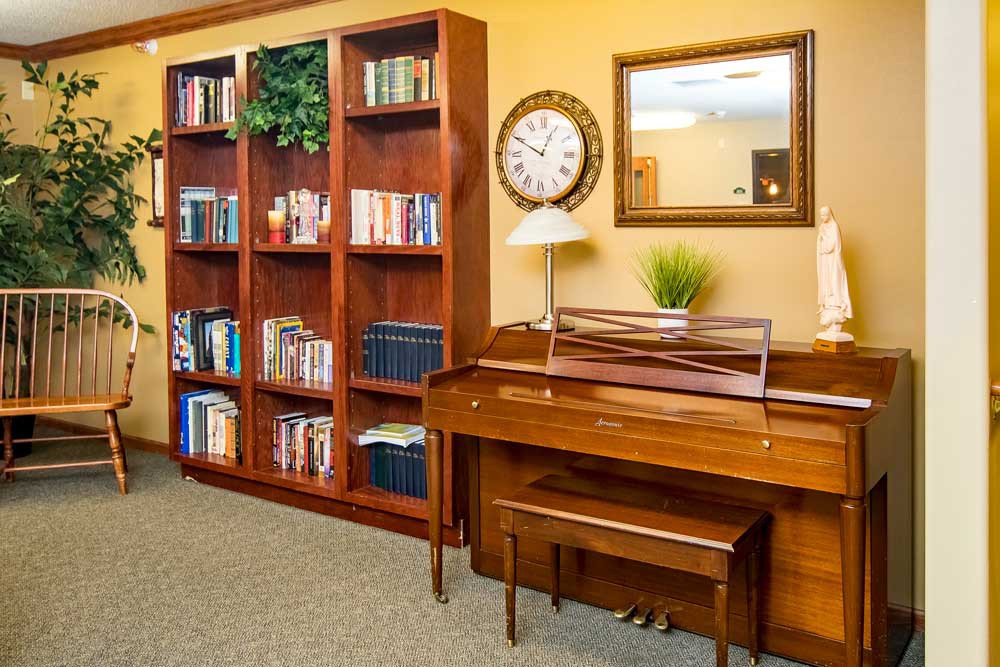 A cozy library corner featuring a wooden bookshelf, a piano, and a decorative clock.
