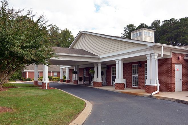 A building with a covered entrance and driveway surrounded by trees.
