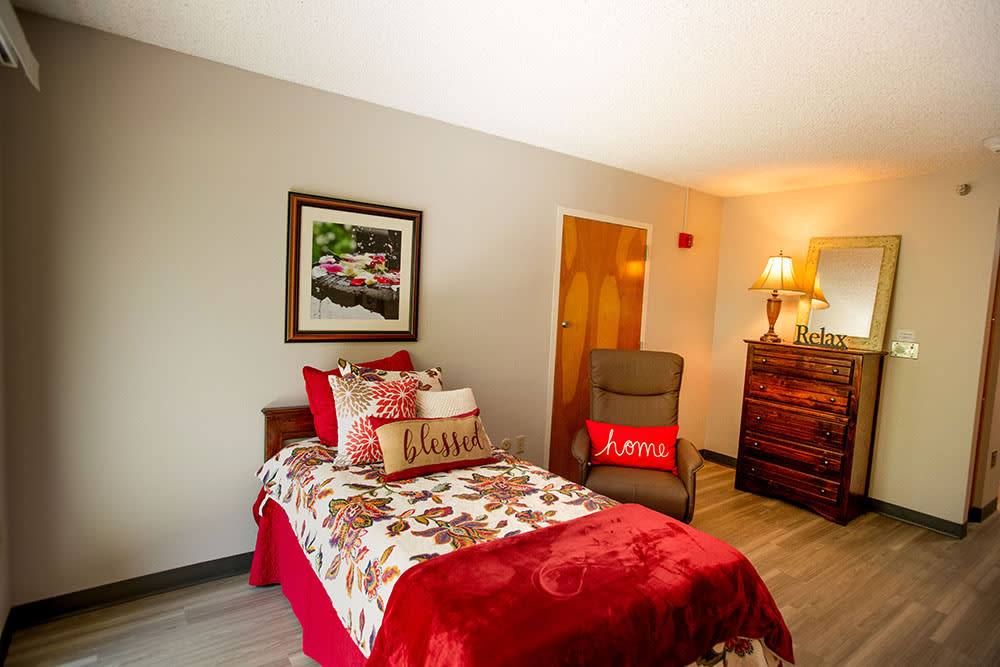 A cozy, well-decorated bedroom featuring a bed with a floral quilt, pillows, and a comfortable armchair.