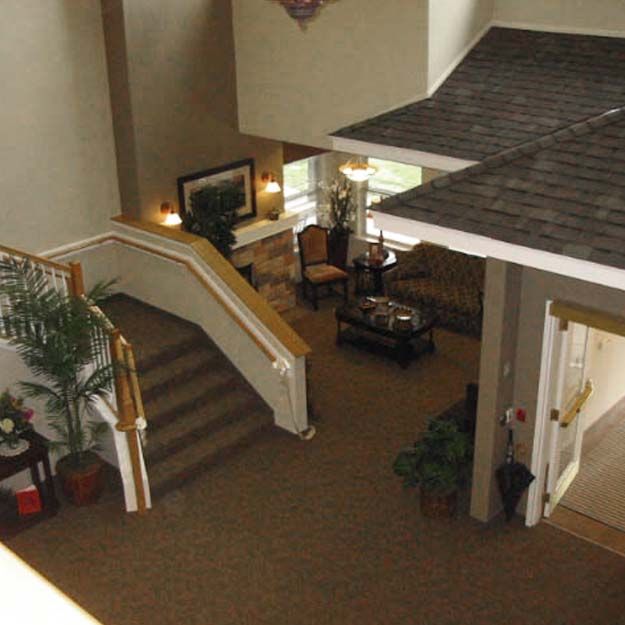 A spacious lobby with carpeted floors, featuring a staircase, potted plants, and a seating area.