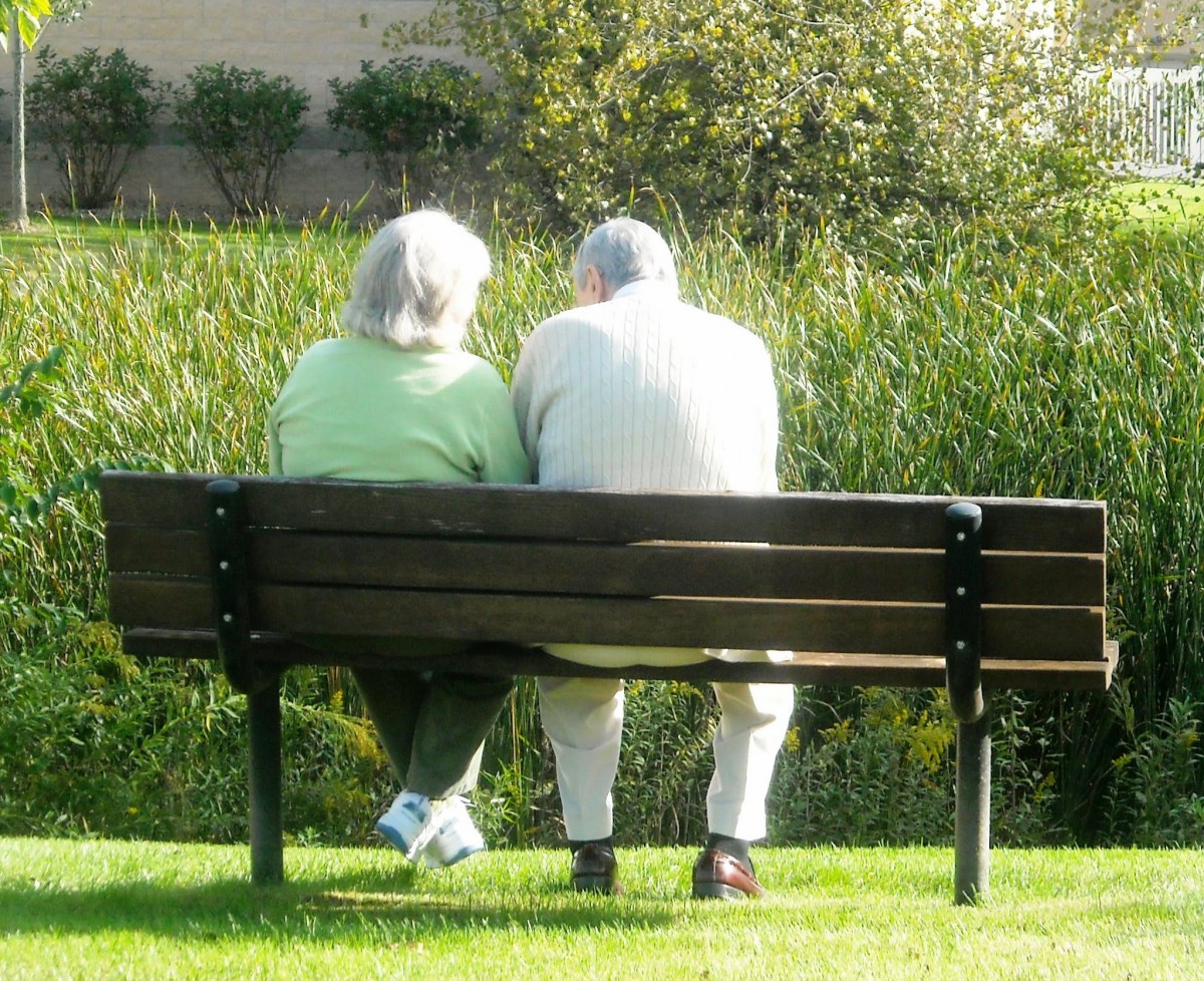 An elderly couple sitting together on a bench in a park, enjoying the outdoors.