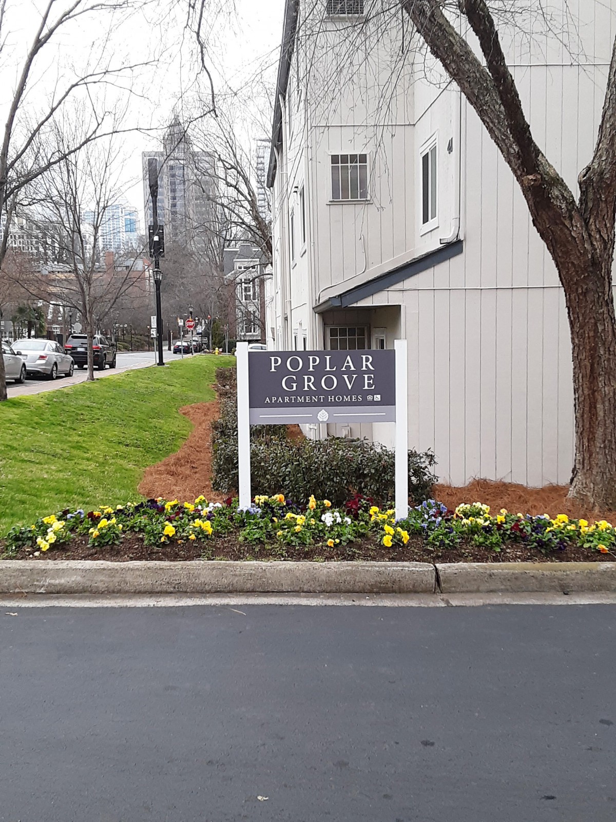 An apartment complex sign surrounded by colorful flowers in an urban setting.
