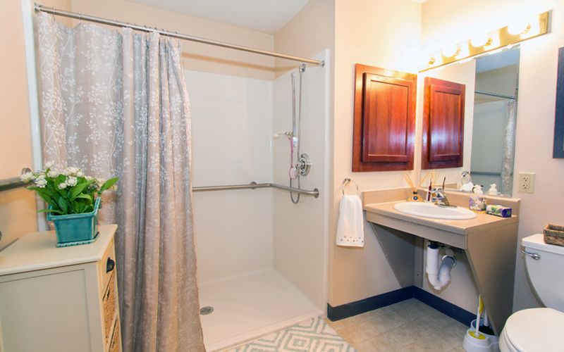 A clean, accessible bathroom with a shower area featuring a handrail, a curtain, and a wide sink with towels.