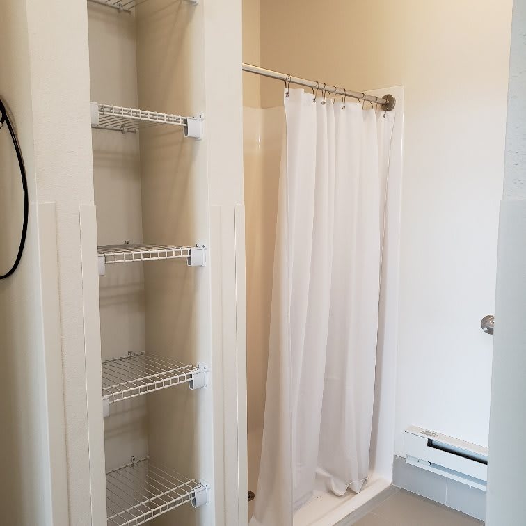 A bathroom with a shower, white curtain, and built-in shelves for storage.