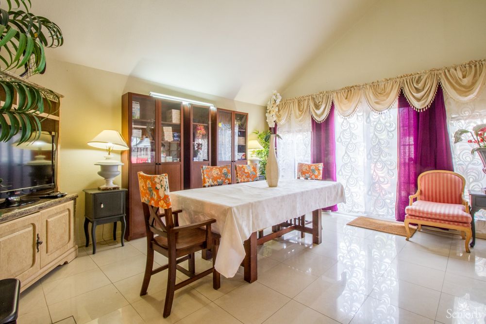 A well-lit dining room with a table, chairs, and a cabinet, featuring elegant decor and curtains.