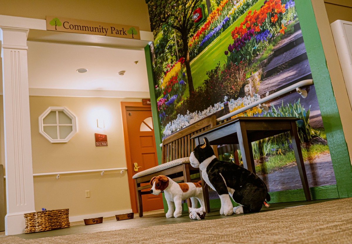 An indoor scene featuring two dog sculptures sitting in front of a bench with a colorful flower mural in the background.