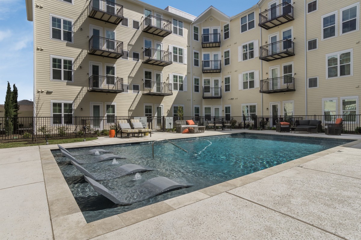 A sunny day at a residential complex featuring a swimming pool and balconies.