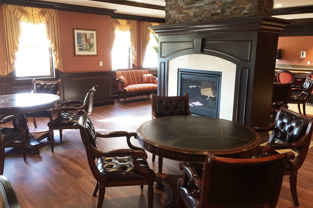 A cozy lounge area featuring a round table with leather chairs, a fireplace, and wooden flooring.