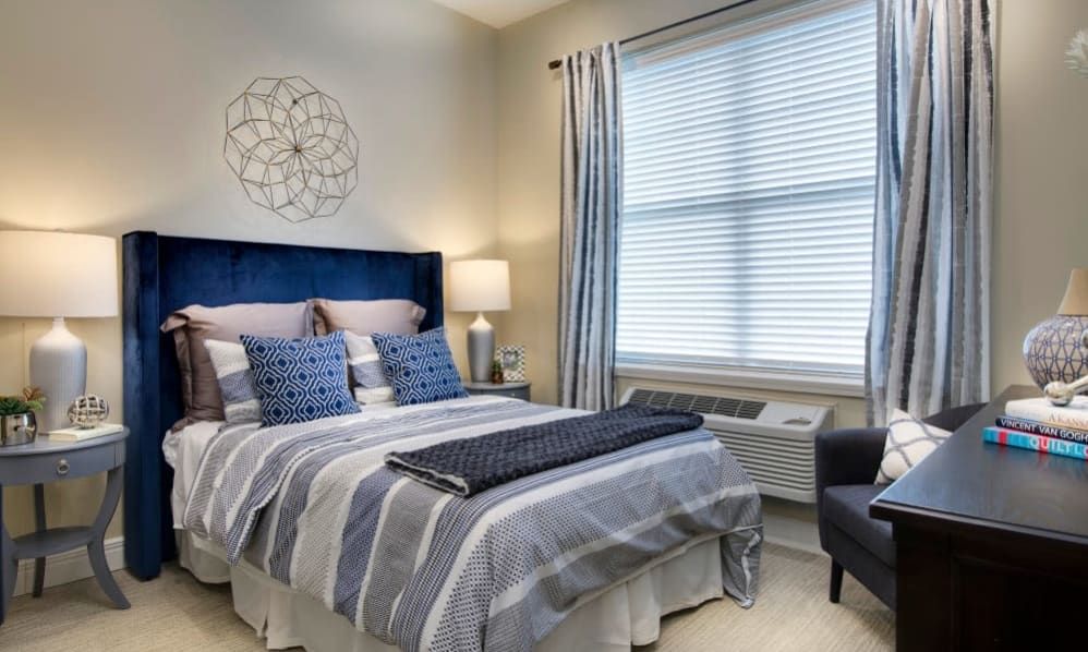 A modern bedroom featuring a comfortable bed with striped bedding, accent pillows, and a stylish lamp near the window.