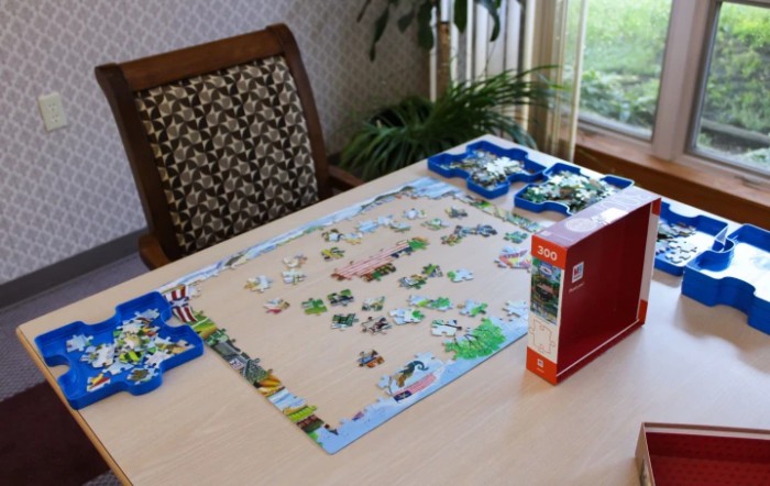A partially completed jigsaw puzzle on a table indoors, surrounded by additional puzzle pieces and a box.