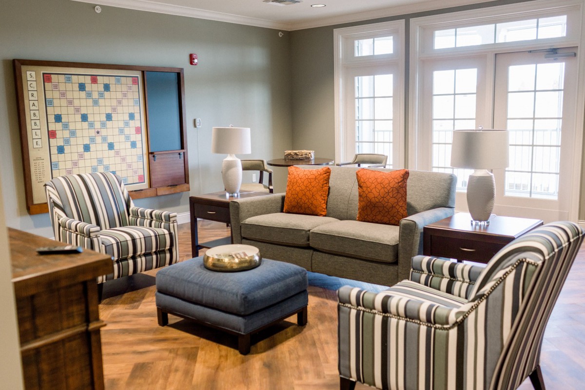 A cozy living room with a sofa, striped armchairs, and a central ottoman surrounded by natural light from large windows.